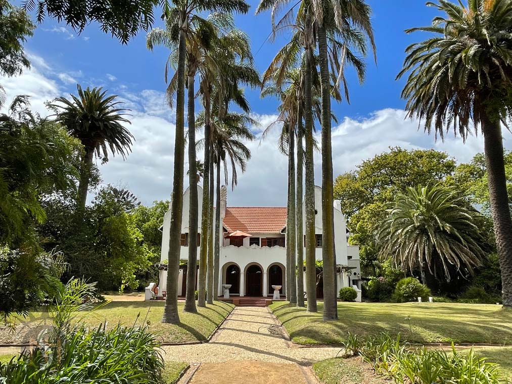Glenhof Manor — home of MANTI, framed by palm trees with a garden path leading to the entrance