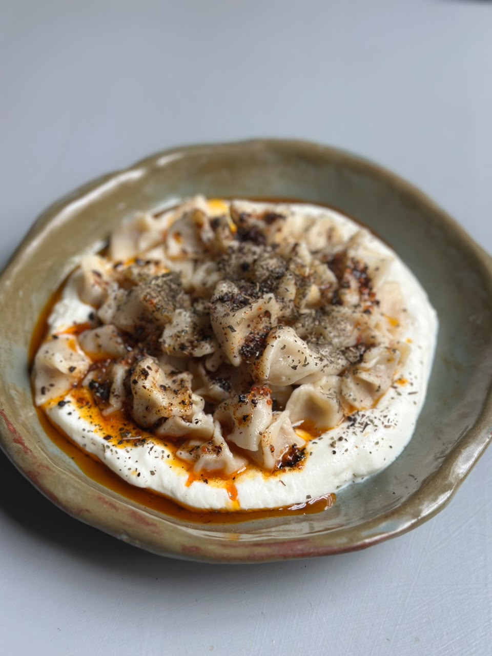 Traditional mantı dumplings on a ceramic plate with garlic yoghurt, Aleppo-spiced browned butter and dried mint